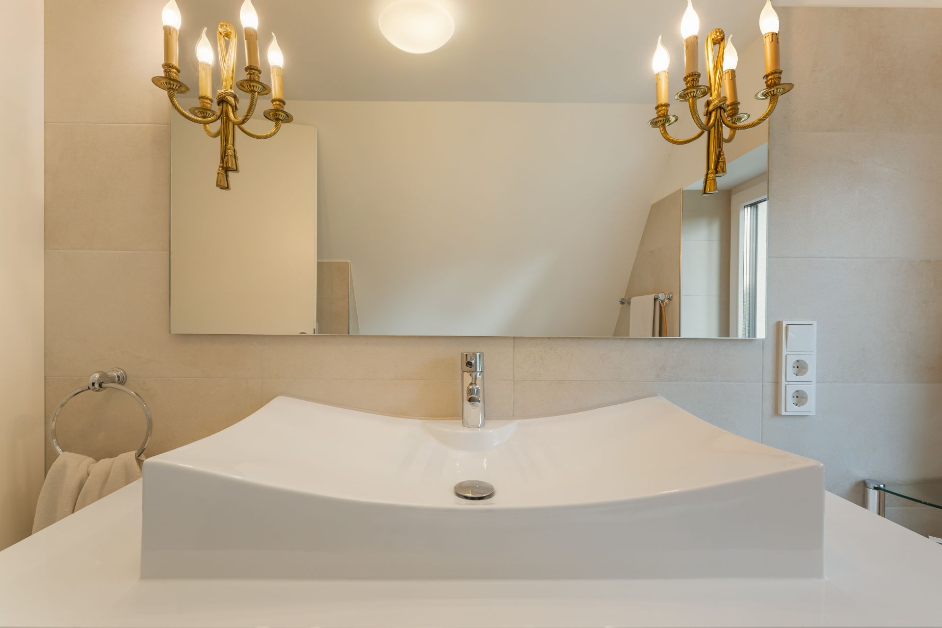 Waschbecken mit großem Spiegel und zwei goldenen Kronleuchtern an der Wand.