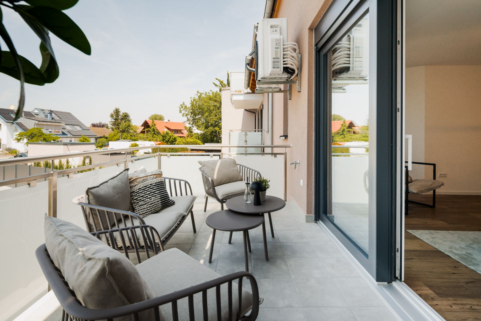Moderner Balkon mit Sitzgruppe, zwei Tischen und Blick auf Nachbarhäuser.