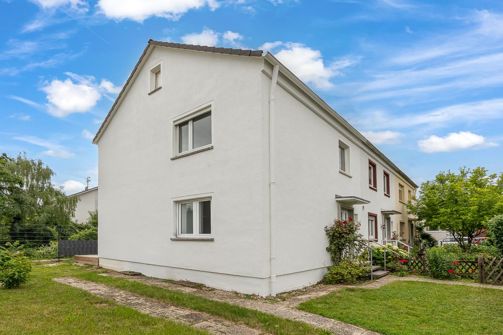 Außenansicht eines weißen Reihenendhauses mit Garten und Gehweg bei blauem Himmel.