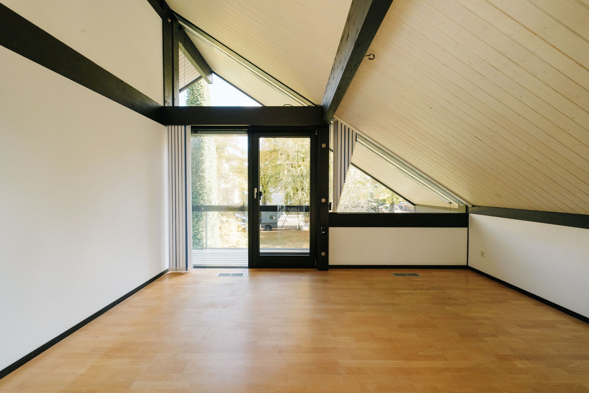 Helles Dachzimmer mit Holzfußboden, großen Fenstern und Glastür zu einem Balkon.
