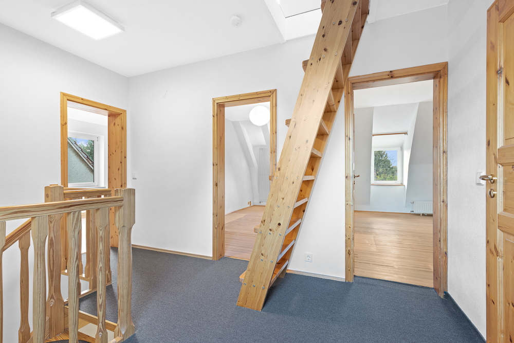 Flur mit Holztreppe nach oben und drei offenen Türen zu hellen Zimmern.