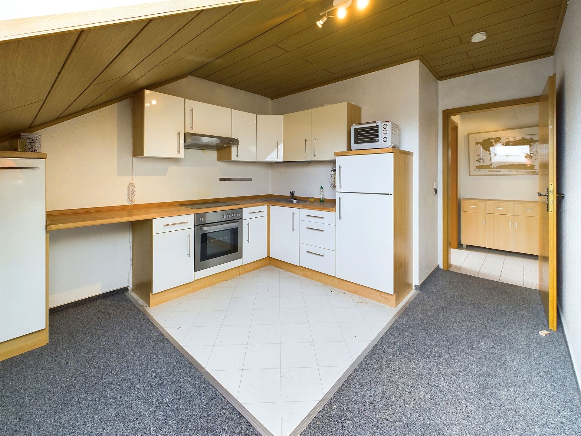Moderne Einbauküche mit weißen Schränken, Backofen, Kühlschrank und Mikrowelle unter Dachschräge.