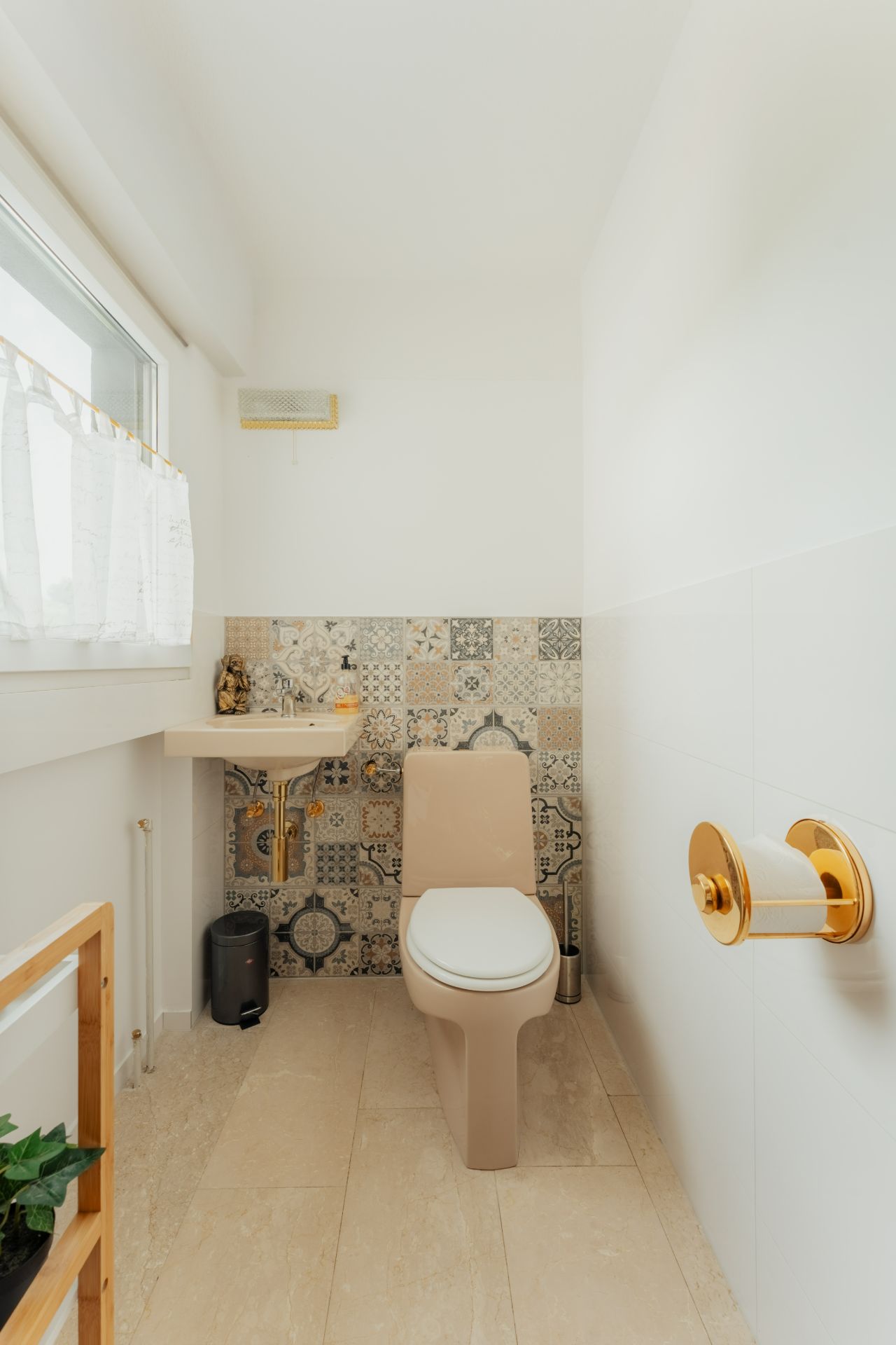 Helles Badezimmer mit beiger Toilette, kleinem Waschbecken und gemusterten Fliesen an der Wand.