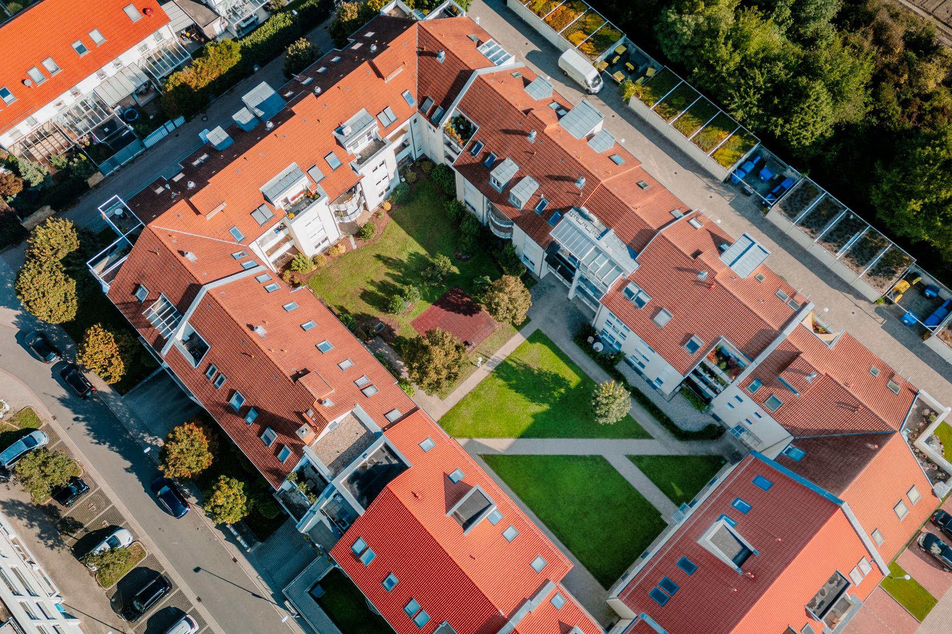 Luftaufnahme eines Wohnkomplexes mit roten Dächern und einem begrünten Innenhof.