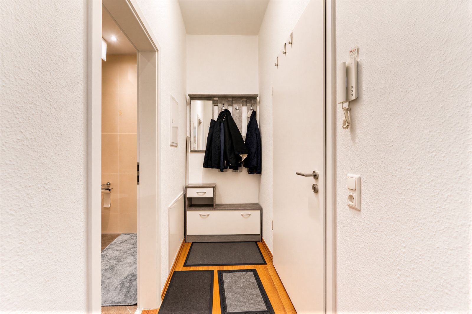 Flur mit Garderobe, Spiegel, Haken, Schuhbank und einigen aufgehängten Jacken.