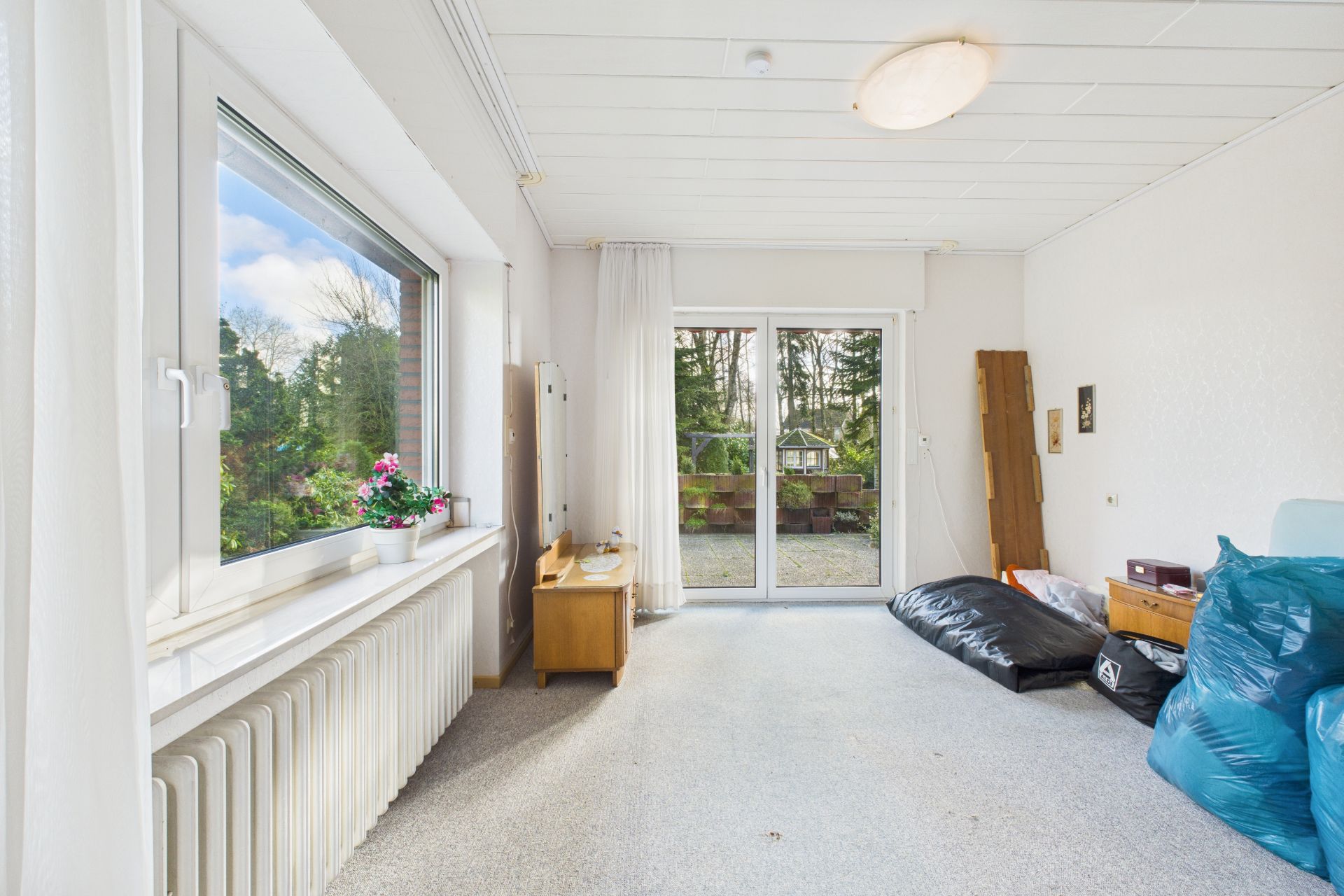 Helles Wohnzimmer mit großem Fenster, Glastür zur Terrasse und wenigen Möbeln.