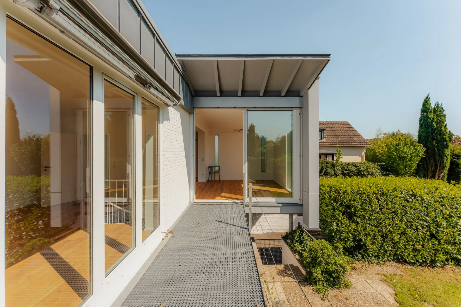 Moderne Terrasse mit großen Fenstern und Blick in den Garten eines Wohnhauses.