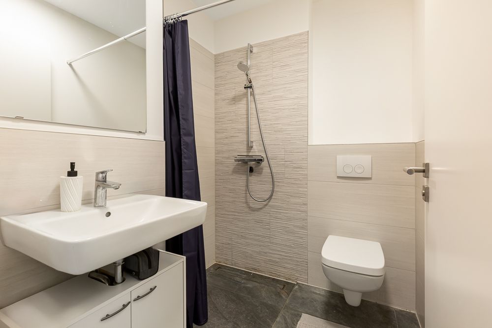 Modernes Badezimmer mit Waschbecken, Spiegel, Dusche und Wandtoilette.