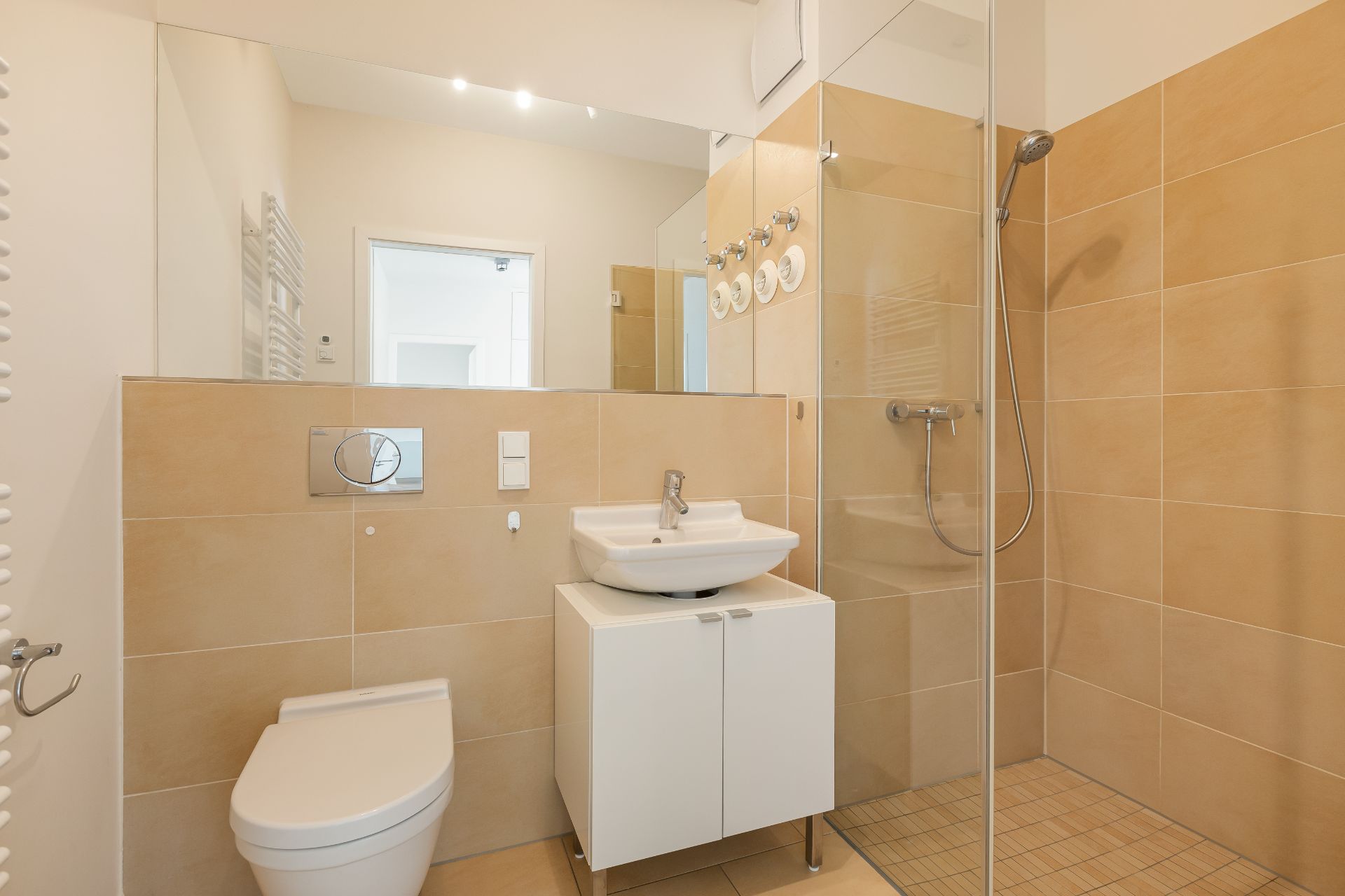 Modernes Badezimmer mit Toilette, Waschbecken und bodengleicher Dusche mit Glaswand.