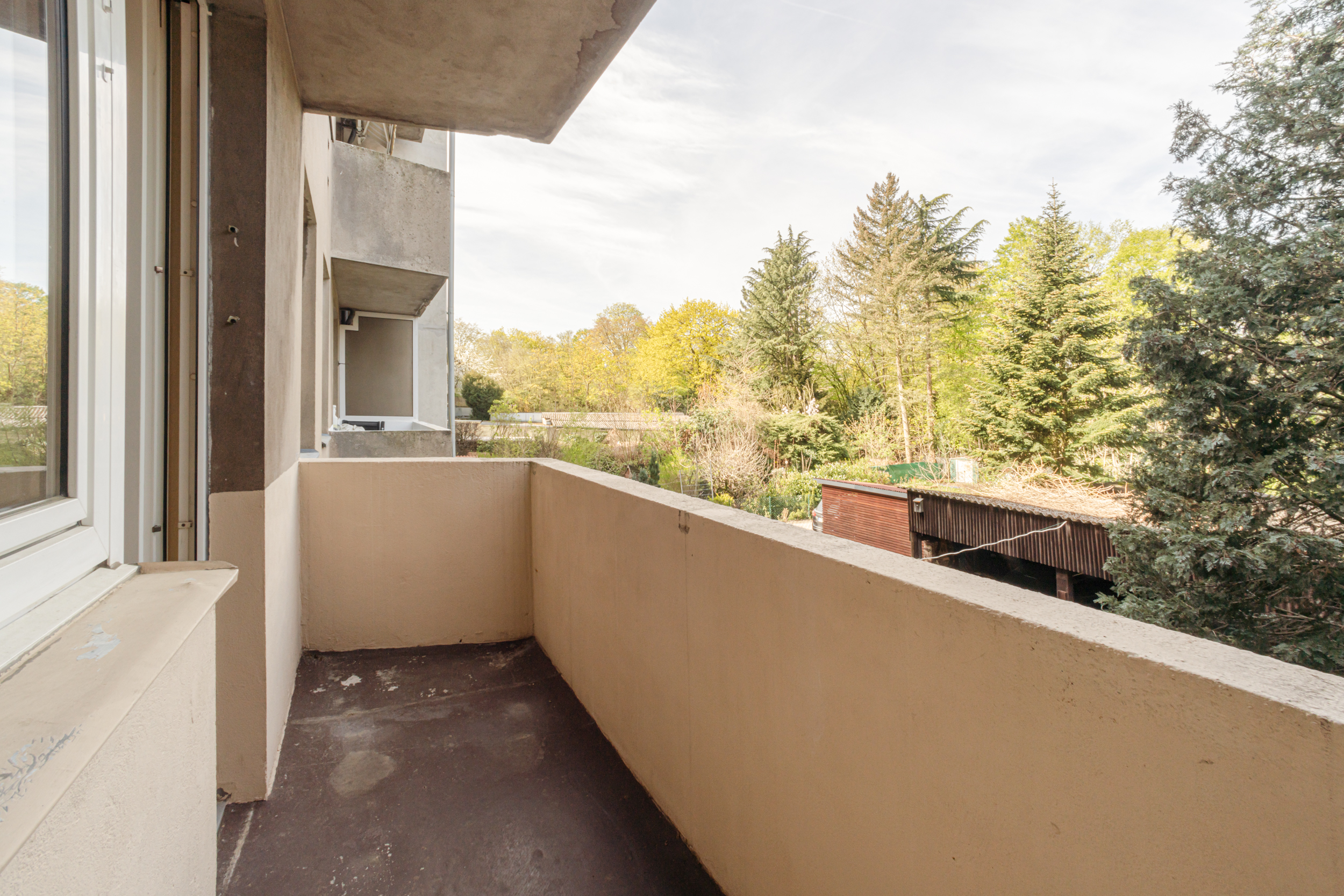 Balkon mit Blick auf einen grünen Garten und umliegende Bäume.