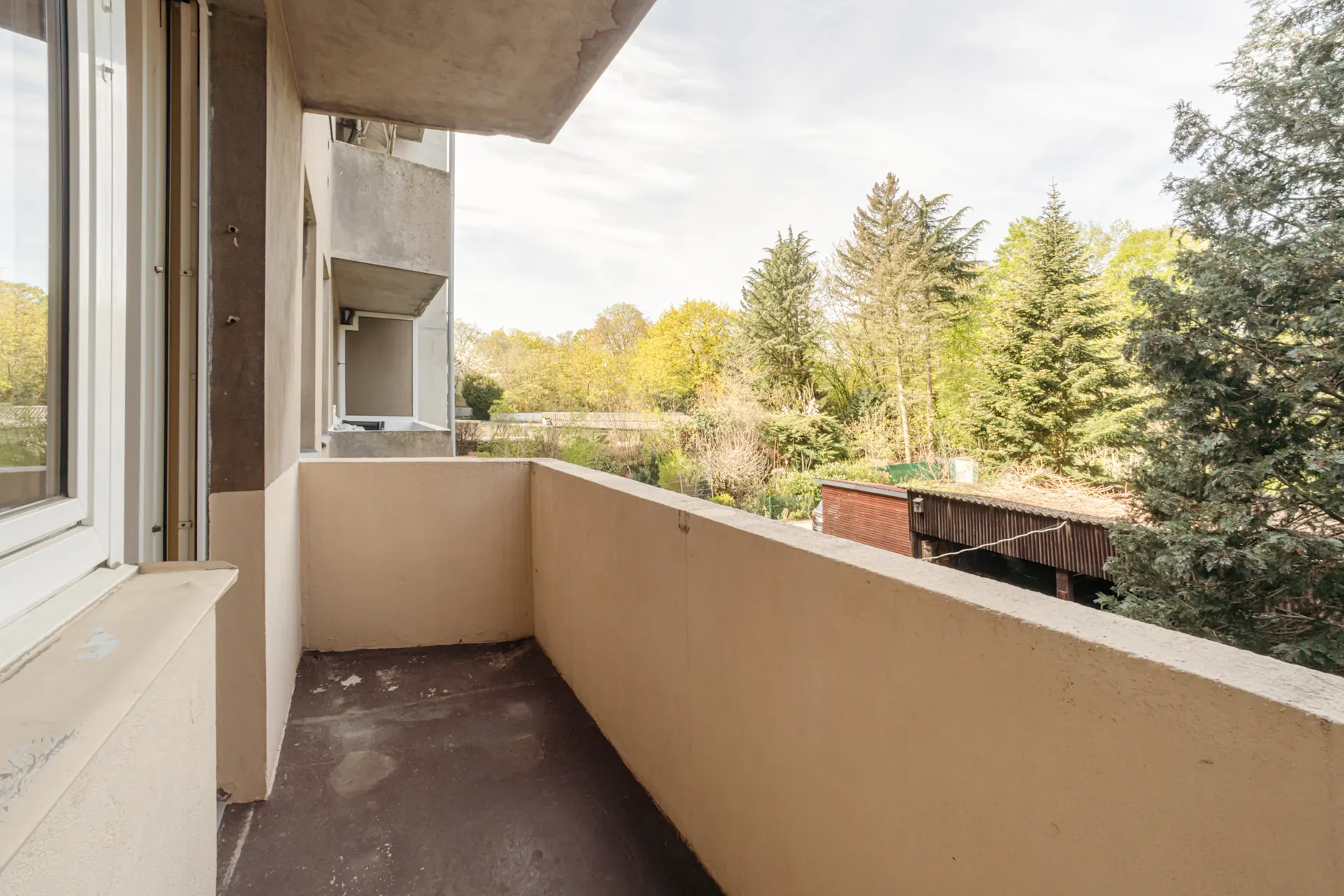 Balkon mit Blick auf einen grünen Garten und umliegende Bäume.