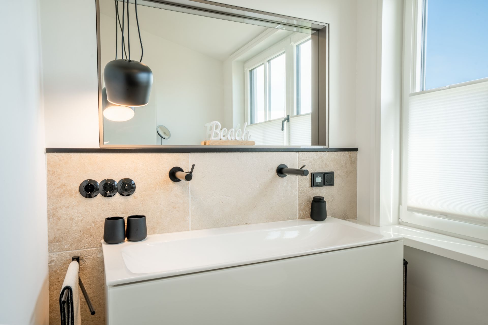 Modernes Badezimmer mit großem Spiegel, Waschbecken, Hängelampe und Fenster mit Rollladen.