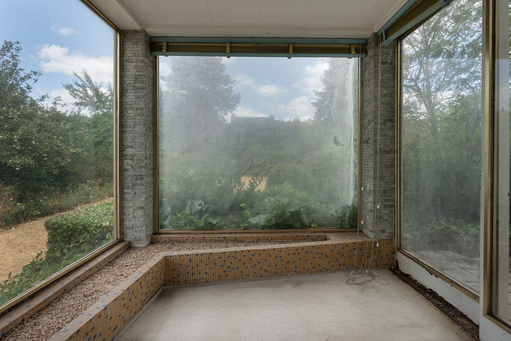 Veranda mit großen Fenstern, Fliesenbank und Blick auf den Garten.