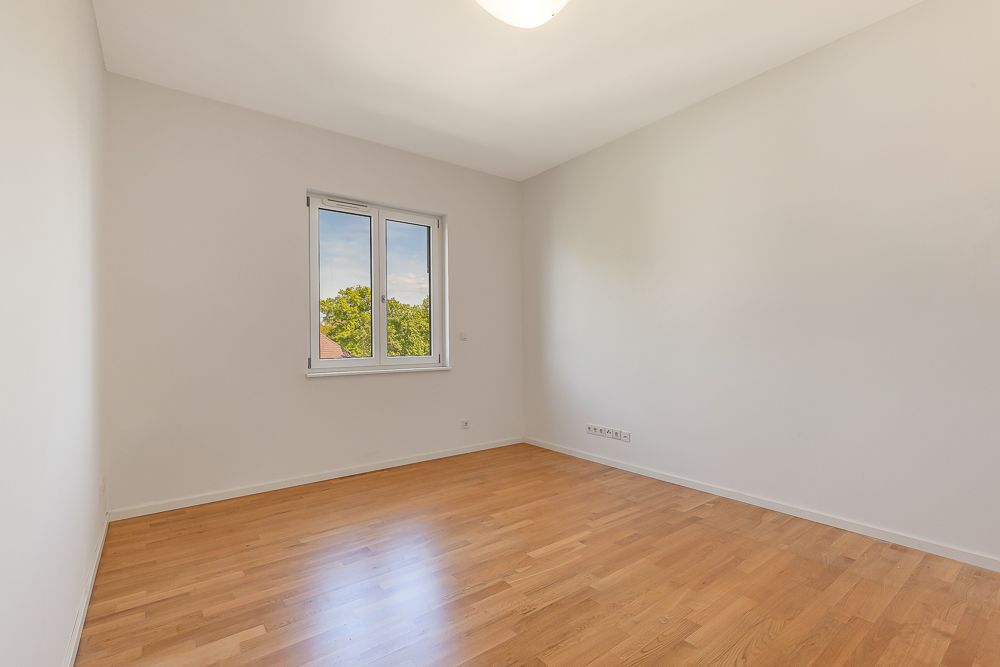 Leeres Zimmer mit Holzfußboden, weißen Wänden und Fenster mit Blick ins Grüne.