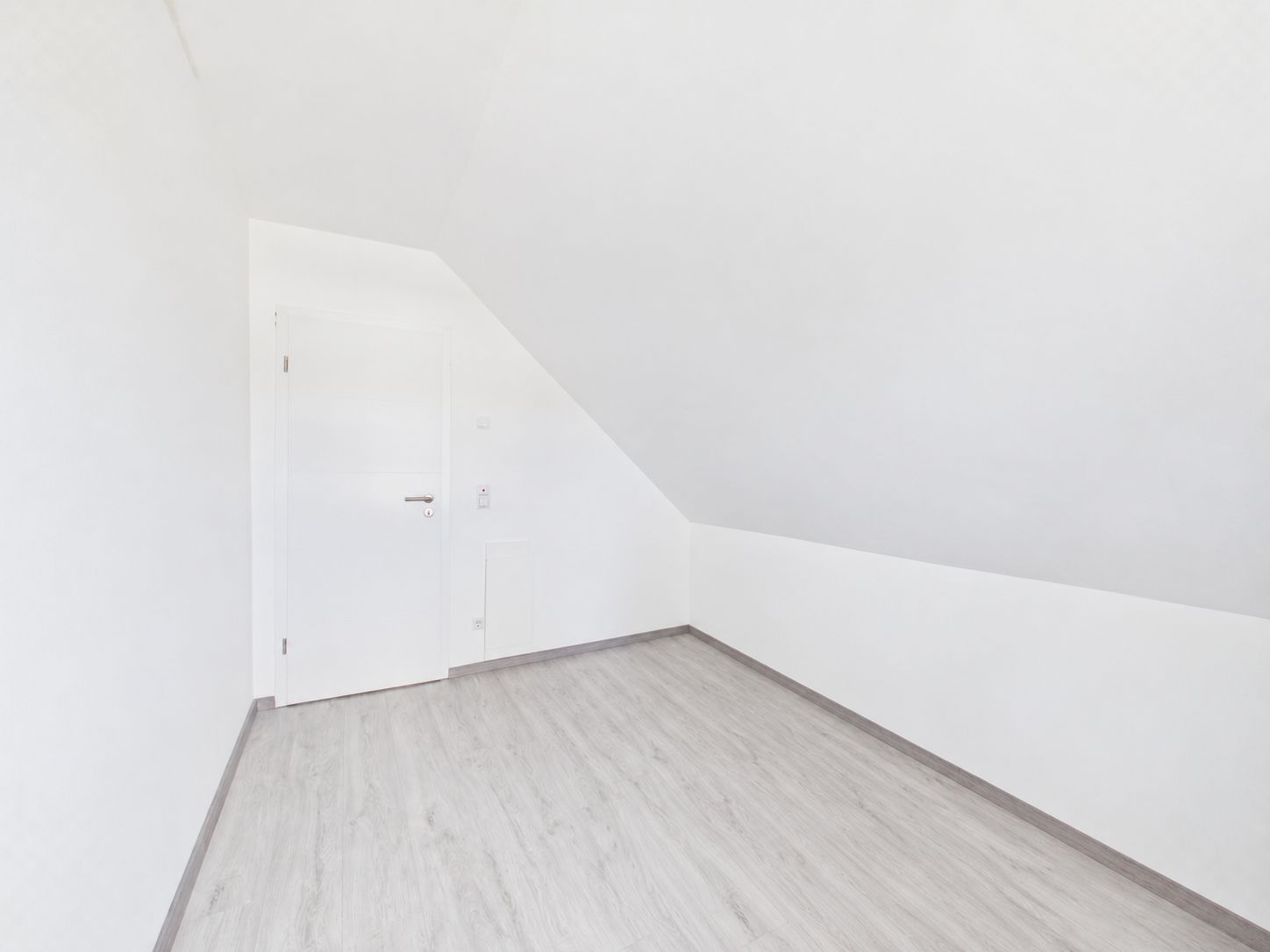 Helles, leeres Zimmer mit Dachschräge, weißem Anstrich und heller Bodenfläche.
