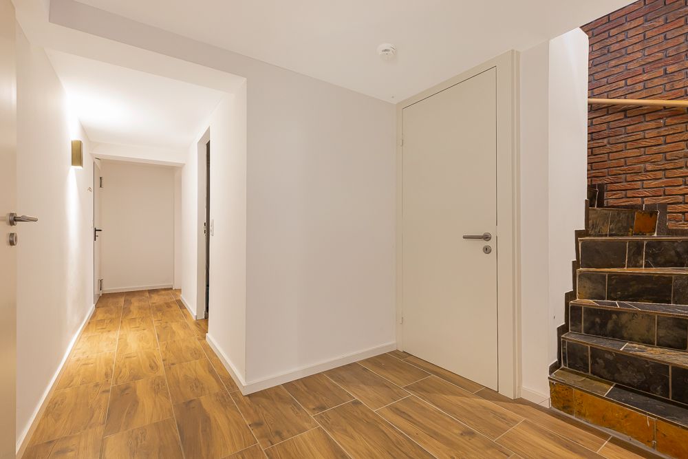 Heller Flur mit Holzboden, weißen Wänden und dunkler Steintreppe.