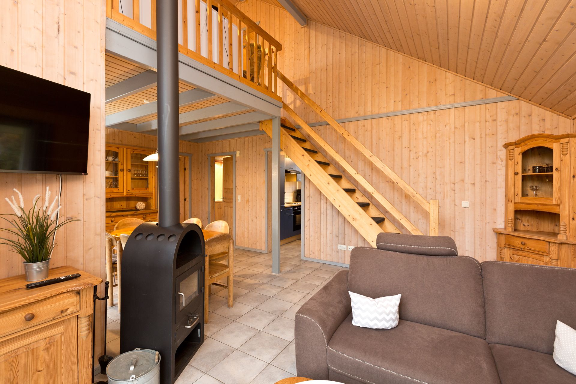 Wohnzimmer mit Holzofen, braunem Sofa, Holztreppe und Holzmöbeln in einem Raum mit Holzvertäfelung.