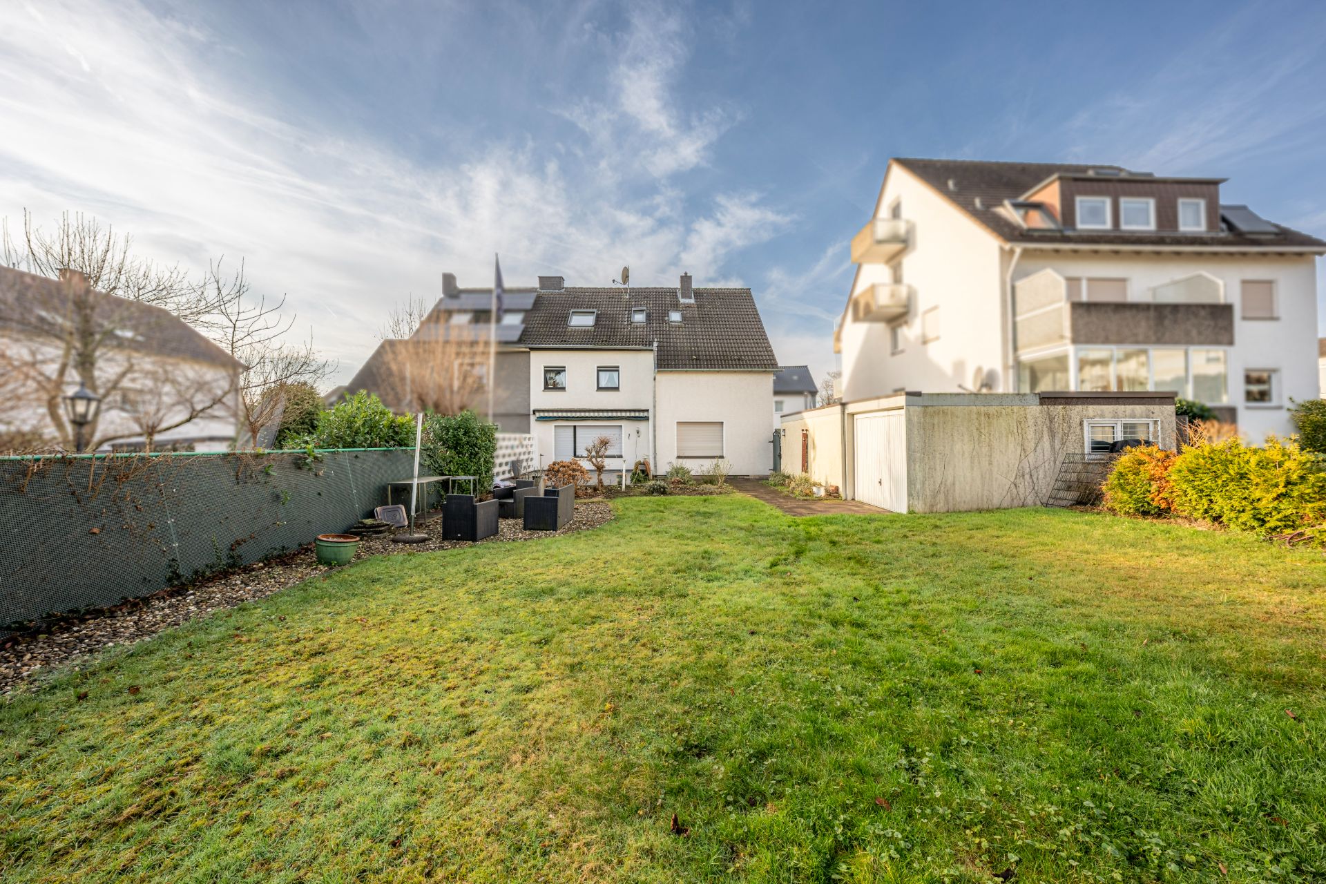 Großer grüner Garten hinter einem Wohnhaus mit angrenzender Garage und Zaun.