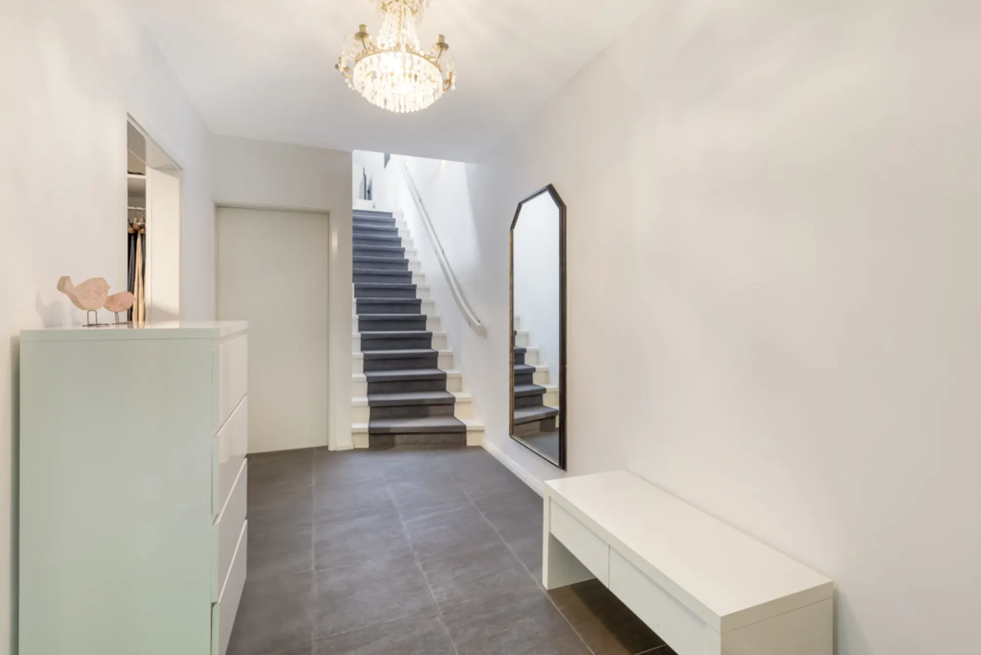 Heller Flur mit Treppe, Spiegel, Kommode und Bank, darüber ein Kronleuchter.