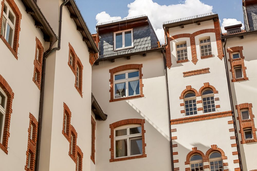 Fassade eines Wohngebäudes mit weißen Wänden und roten Ziegelumrandungen an den Fenstern.