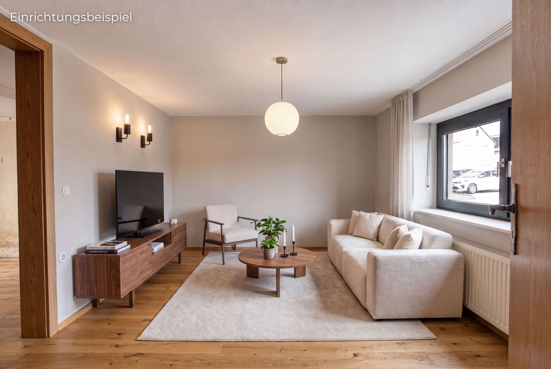 Helles Wohnzimmer mit Sofa, TV, Couchtisch, Sessel und großem Fenster.