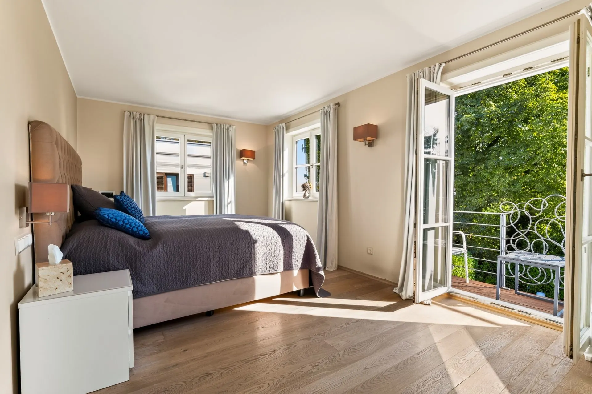 Helles Schlafzimmer mit Doppelbett, Holzfußboden und Balkonzugang durch geöffnete Glastüren.