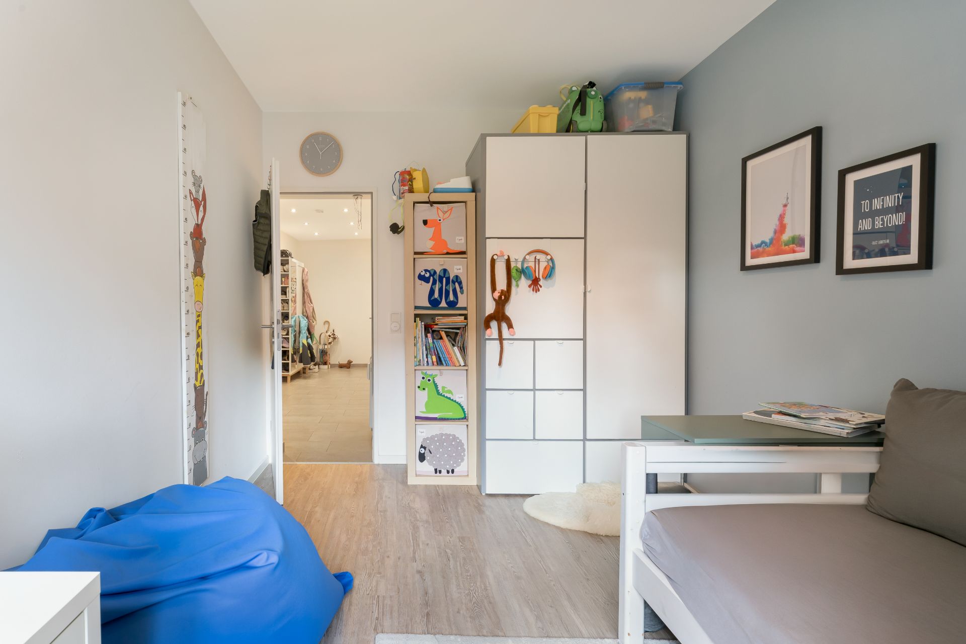 Kinderzimmer mit Schrank, Regal, Sofa und blauem Sitzsack, hellem Boden und Wandbildern.