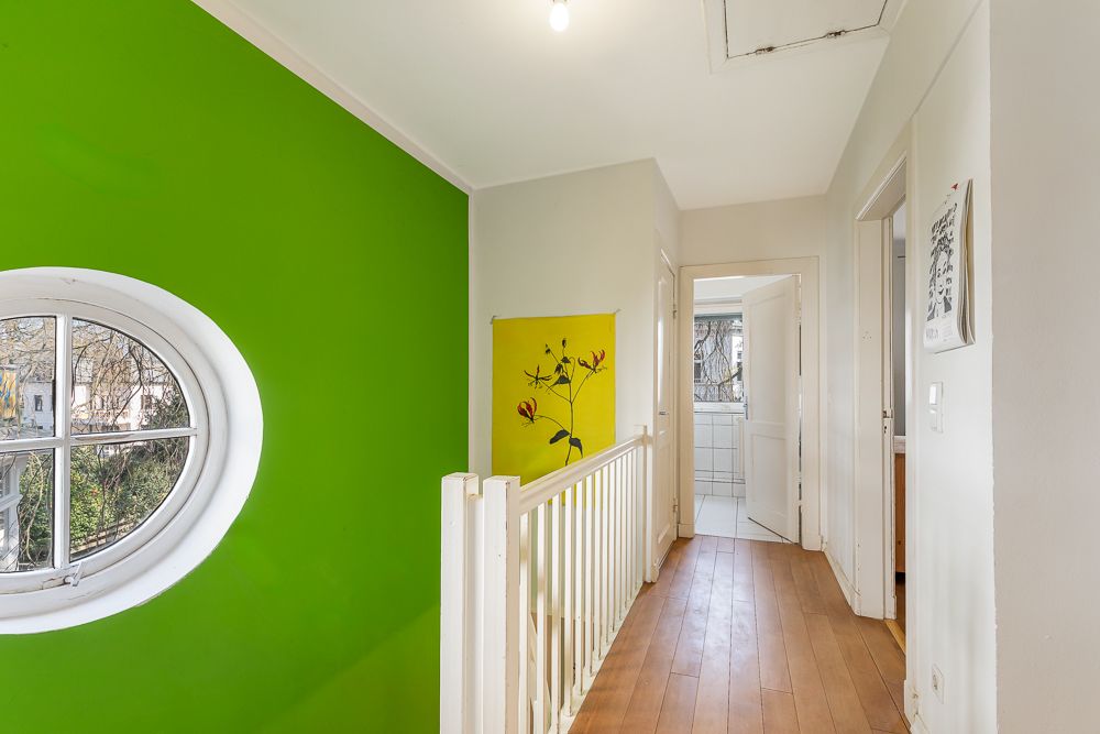 Heller Flur mit grüner Wand, rundem Fenster und Holzfußboden in einem Wohnhaus.