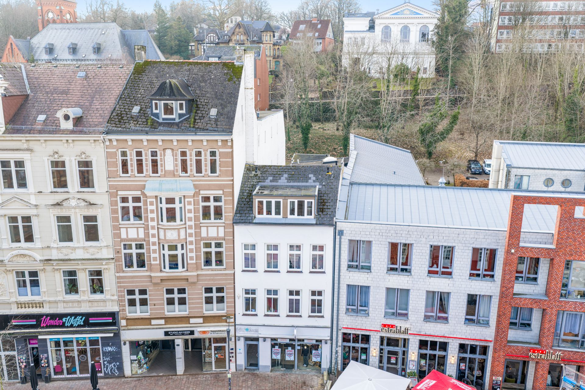 Drei mehrstöckige Wohnhäuser mit Geschäften im Erdgeschoss in einer städtischen Straße.