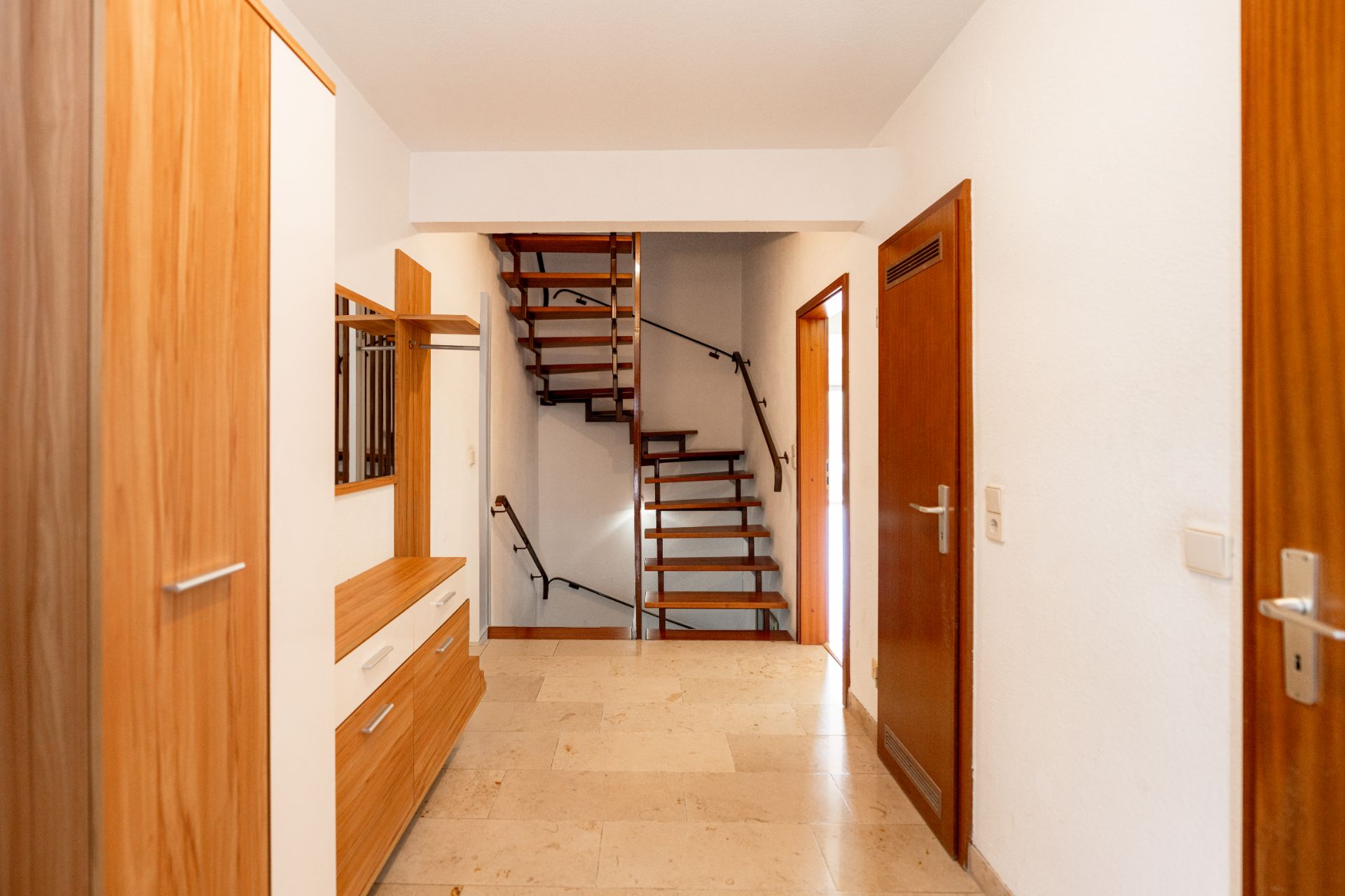 Flur mit Holzschränken und offener Holztreppe im Hintergrund.