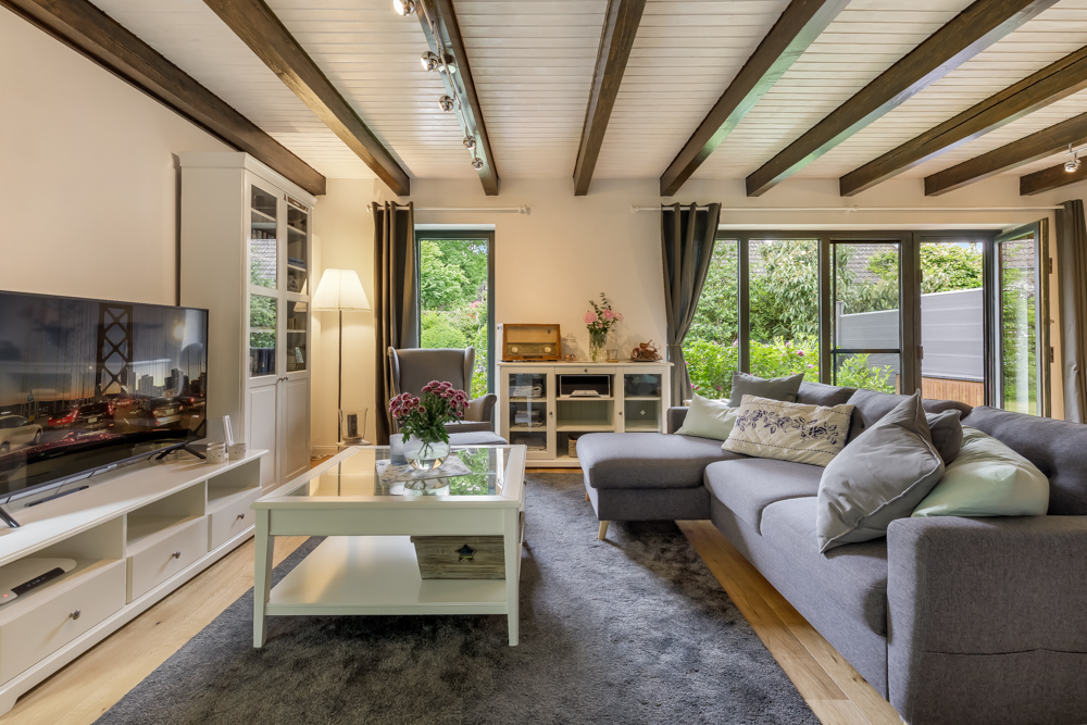 Helles Wohnzimmer mit grauem Sofa, Couchtisch, Fernseher und Blick in den Garten.