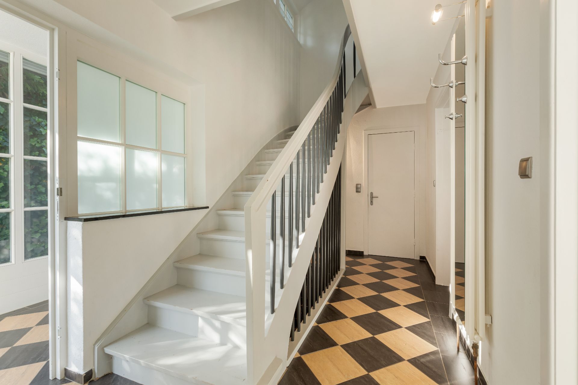 Heller Flur mit schwarz-weiß kariertem Boden und weißer Treppe nach oben.