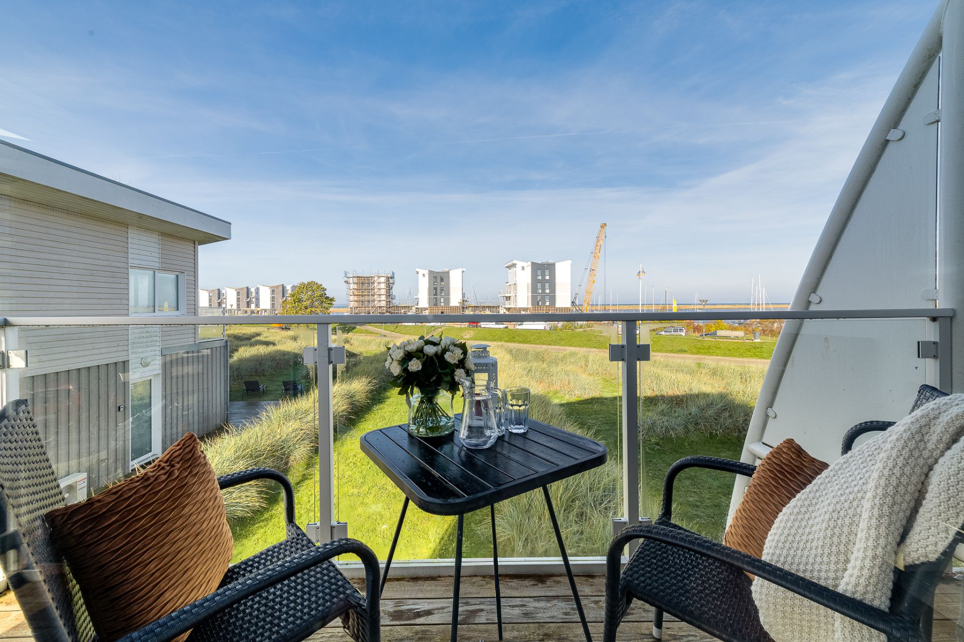 Balkon mit zwei Stühlen, Tisch mit Blumen und Gläsern, Blick auf Grünfläche und moderne Gebäude.