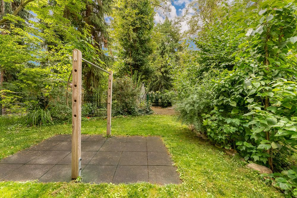 Grüner Garten mit Klimmzugstange auf Gummiplatten, umgeben von Bäumen und Büschen.
