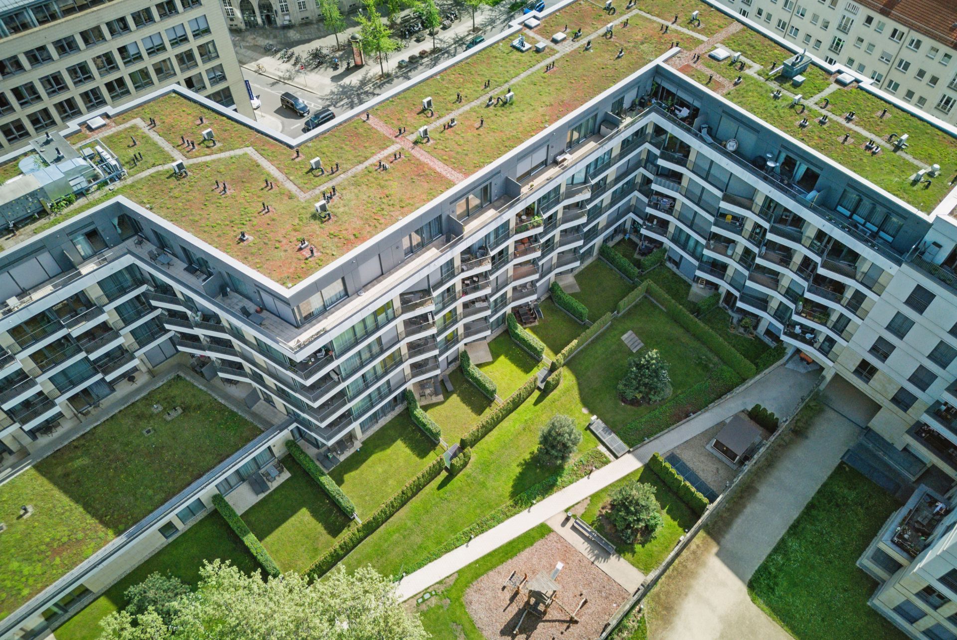 L-förmiges Wohngebäude mit begrüntem Dach und Innenhof mit Wegen und Spielplatz.