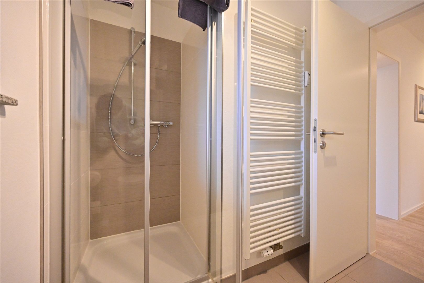 Dusche mit Glastüren und Handtuchheizkörper in einem modernen Badezimmer.
