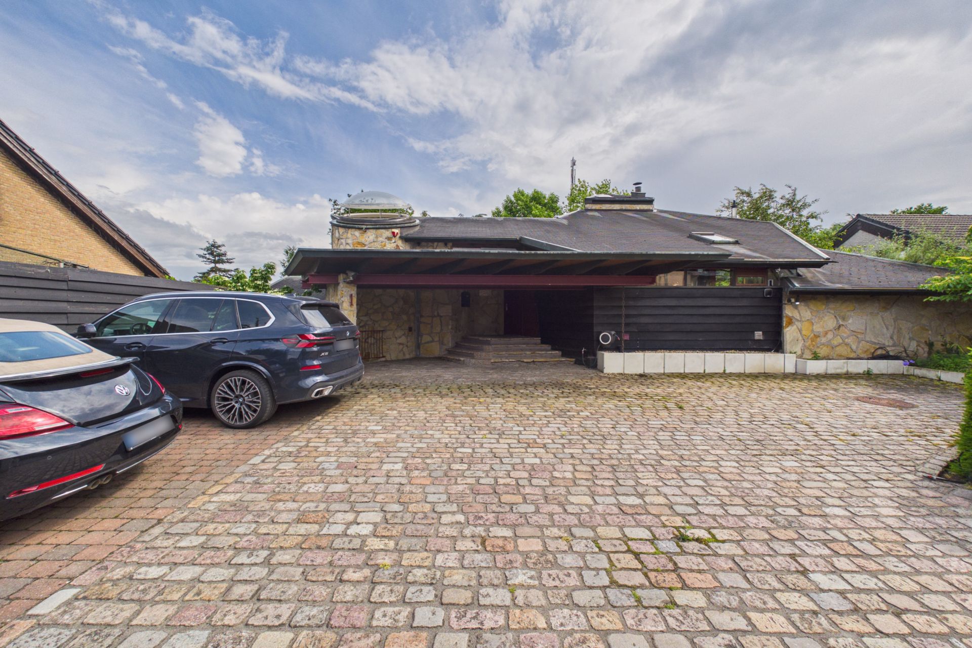 Einfamilienhaus mit Flachdach und zwei Autos auf einem gepflasterten Hof.