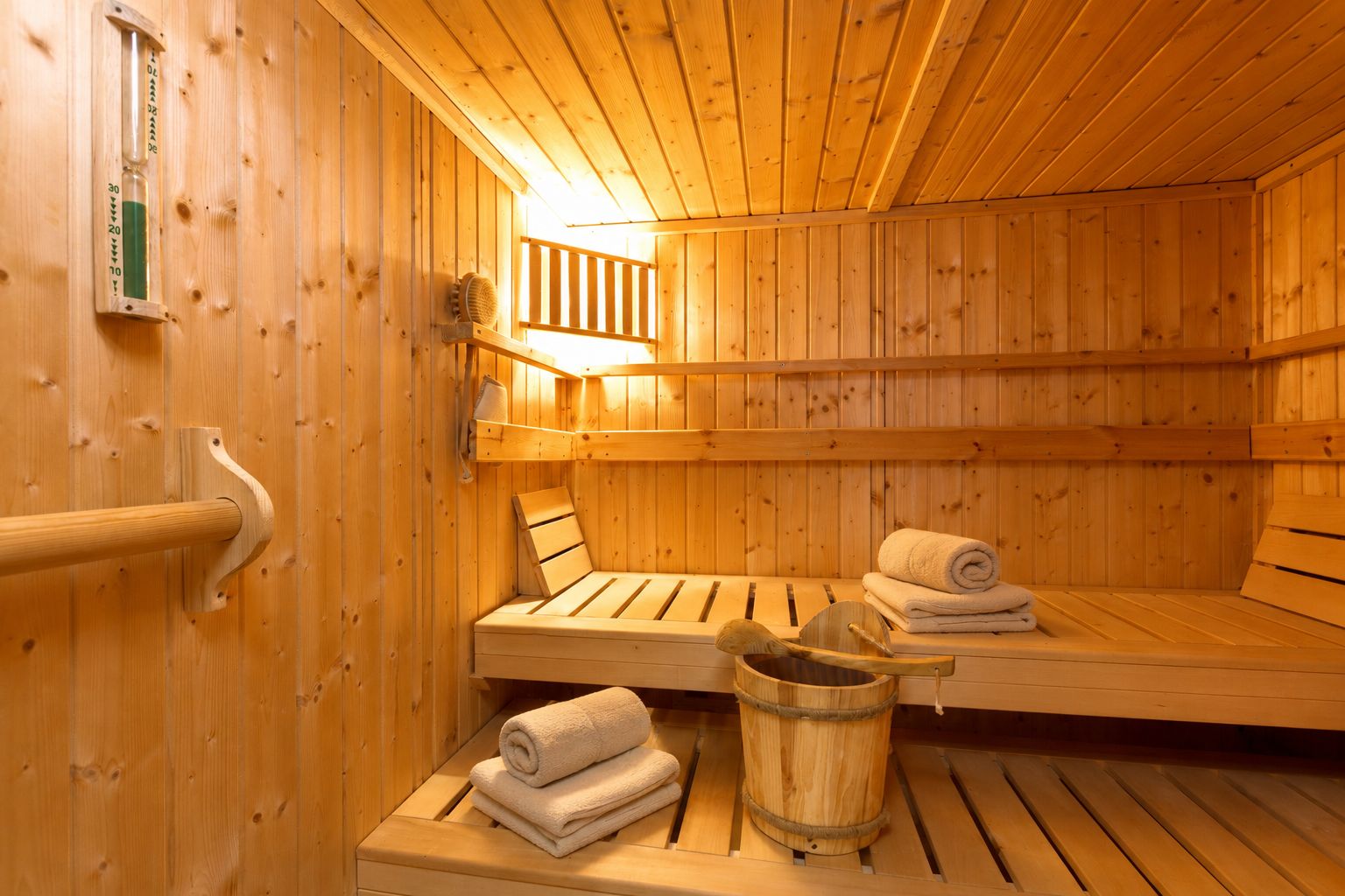 Innenansicht einer Holzsauna mit Bänken, Handtüchern und einem Holzeimer.