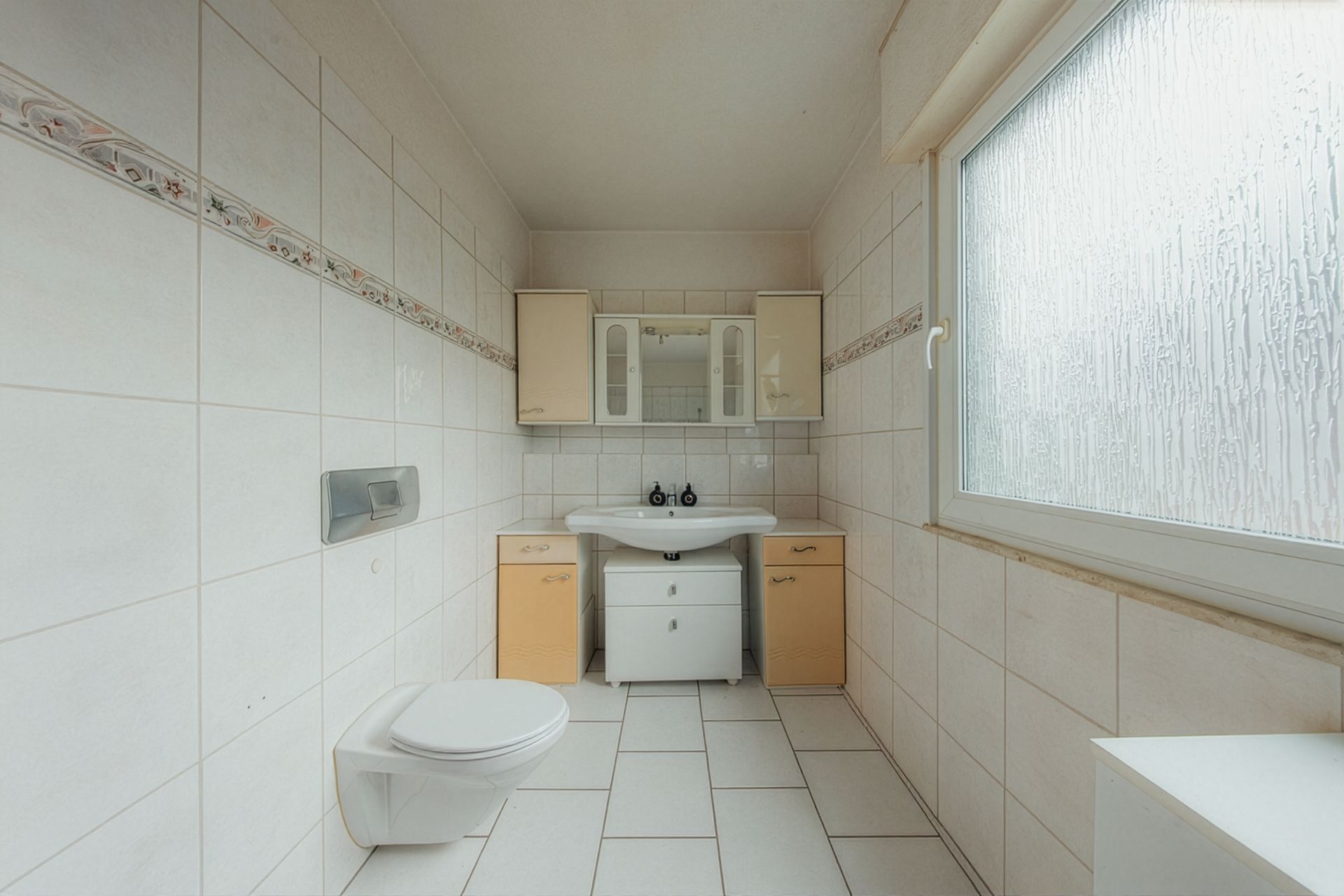 Helles Badezimmer mit Wandtoilette, Waschbecken, Spiegel und großem Fenster.