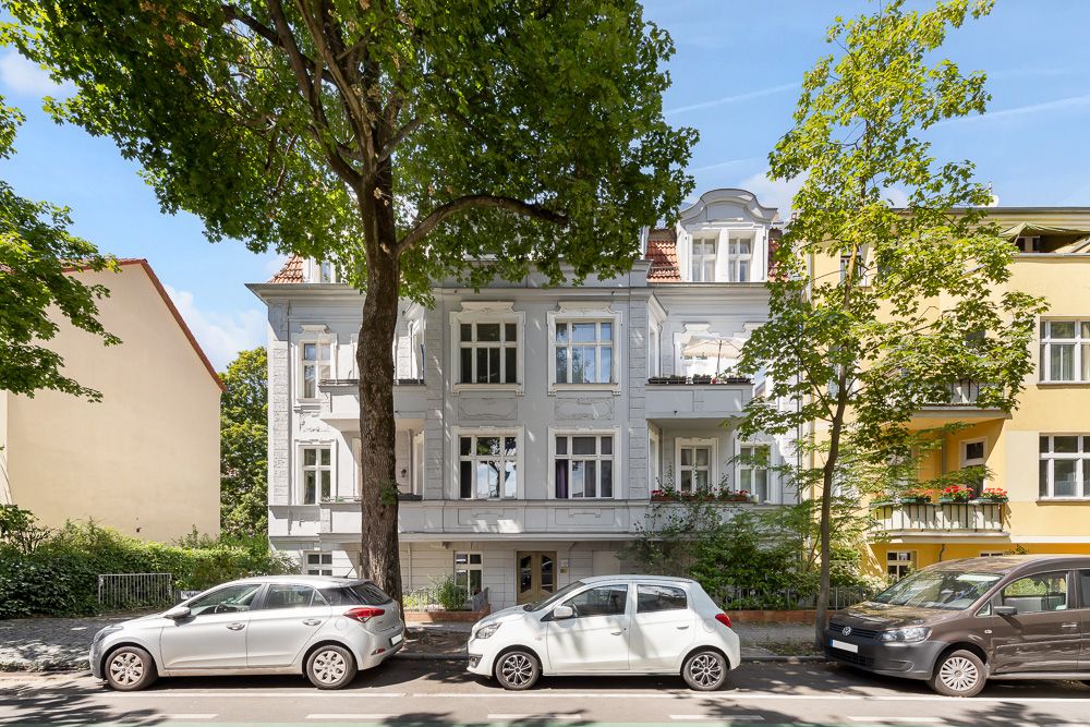 Mehrstöckiges Wohnhaus mit weißen Fassaden, großen Fenstern und parkenden Autos davor.