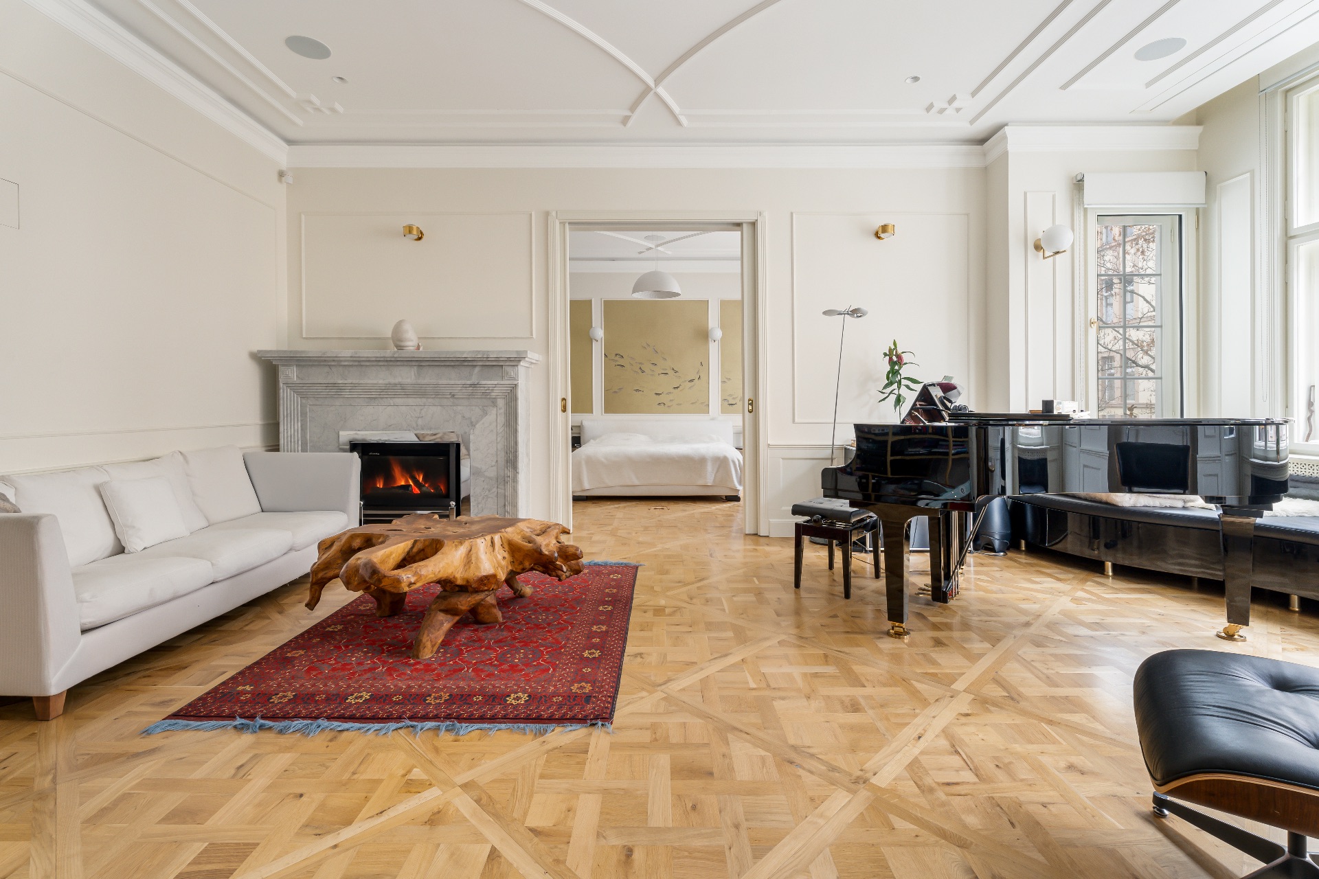 Helles Wohnzimmer mit Kamin, Sofa, Holz-Couchtisch, Klavier und Blick ins Schlafzimmer.
