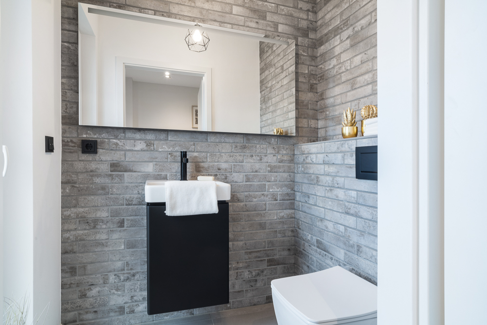 Modernes Badezimmer mit grauen Fliesen, Spiegel, Waschbecken und Toilette.