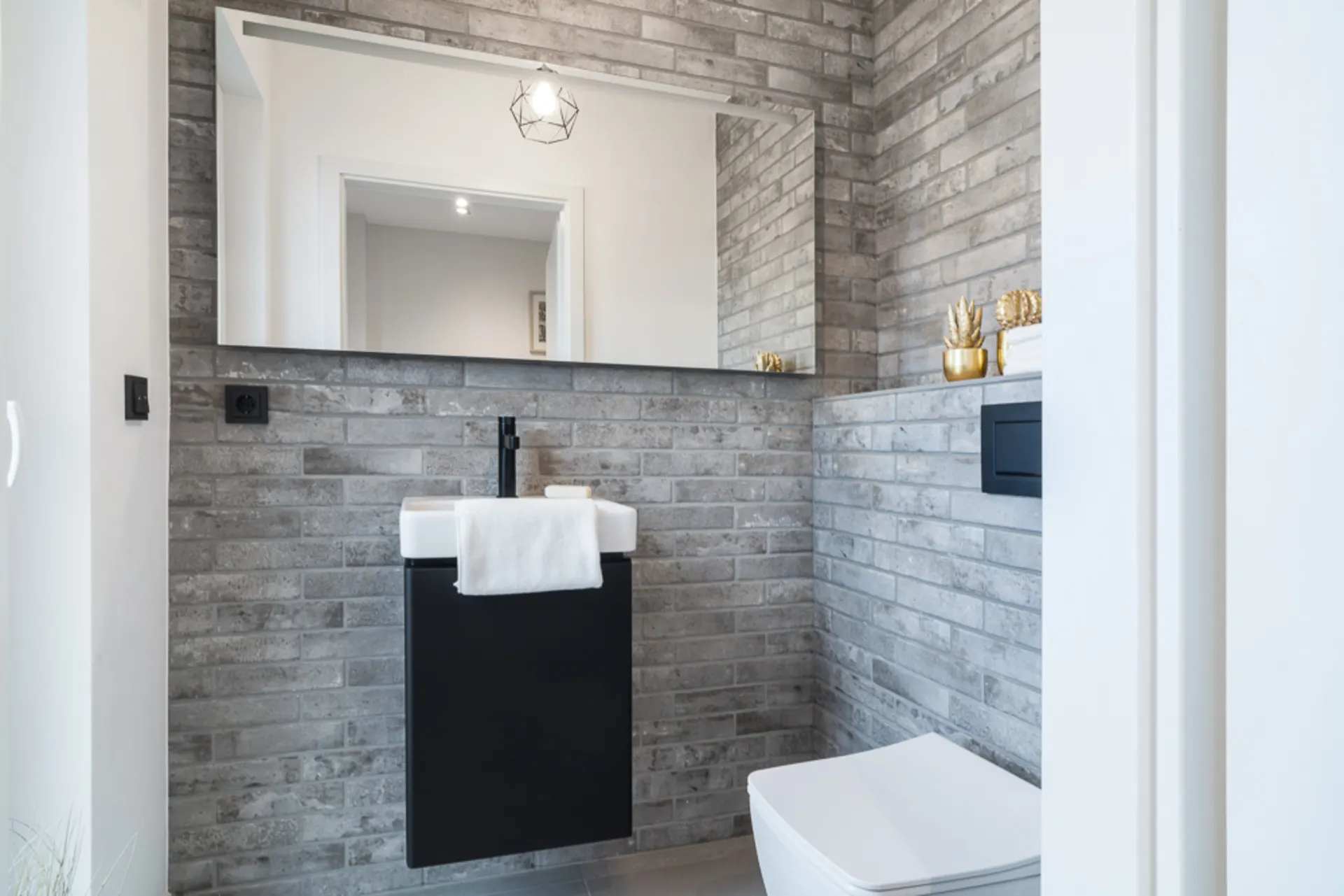 Modernes Badezimmer mit grauen Fliesen, Spiegel, Waschbecken und Toilette.