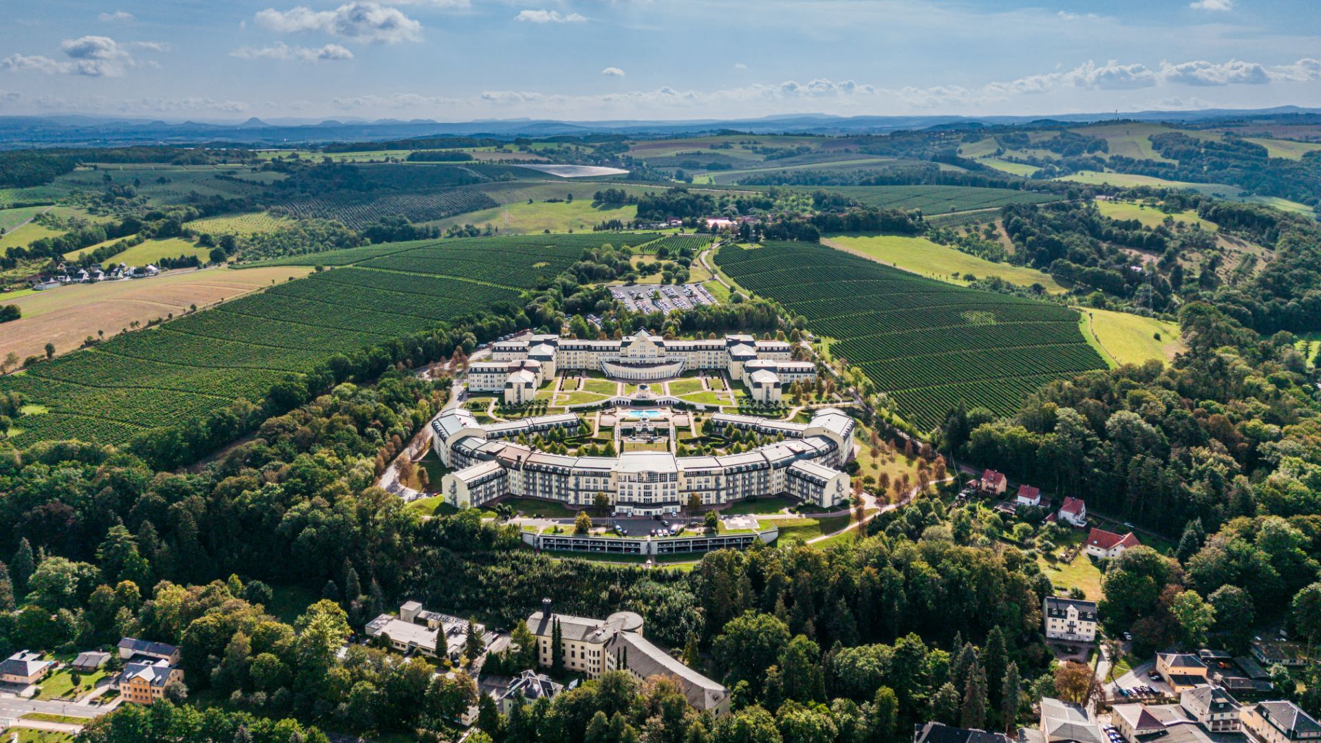 Luftaufnahme eines großen Gebäudekomplexes mit umliegenden Feldern und Wäldern.