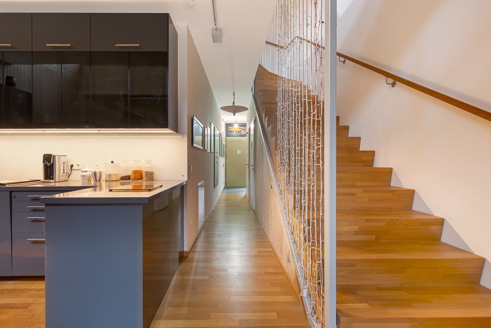 Moderne Küche mit Holzboden und Treppe daneben, Flur mit Bildern an der Wand.