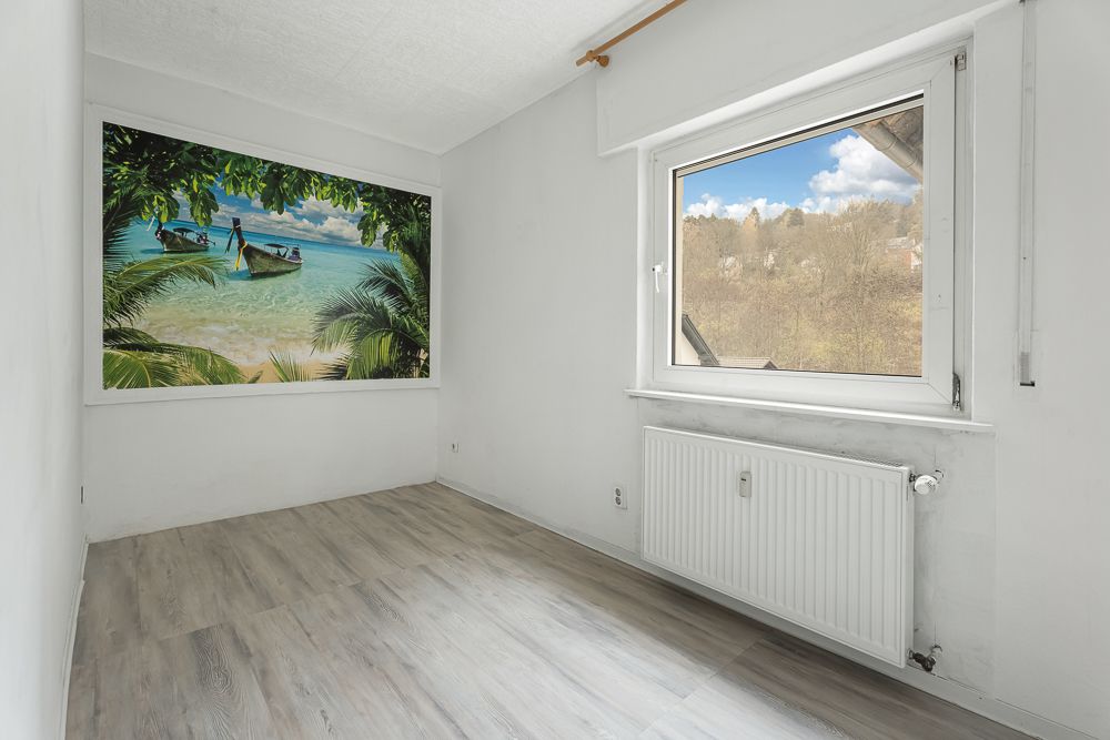 Kleines, leeres Zimmer mit großem Fenster und Wandbild eines Strandes.