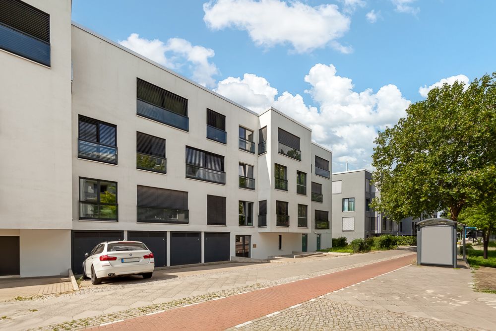 Modernes Wohngebäude mit weißen Fassaden und großen Fenstern, geparktes Auto vorne.