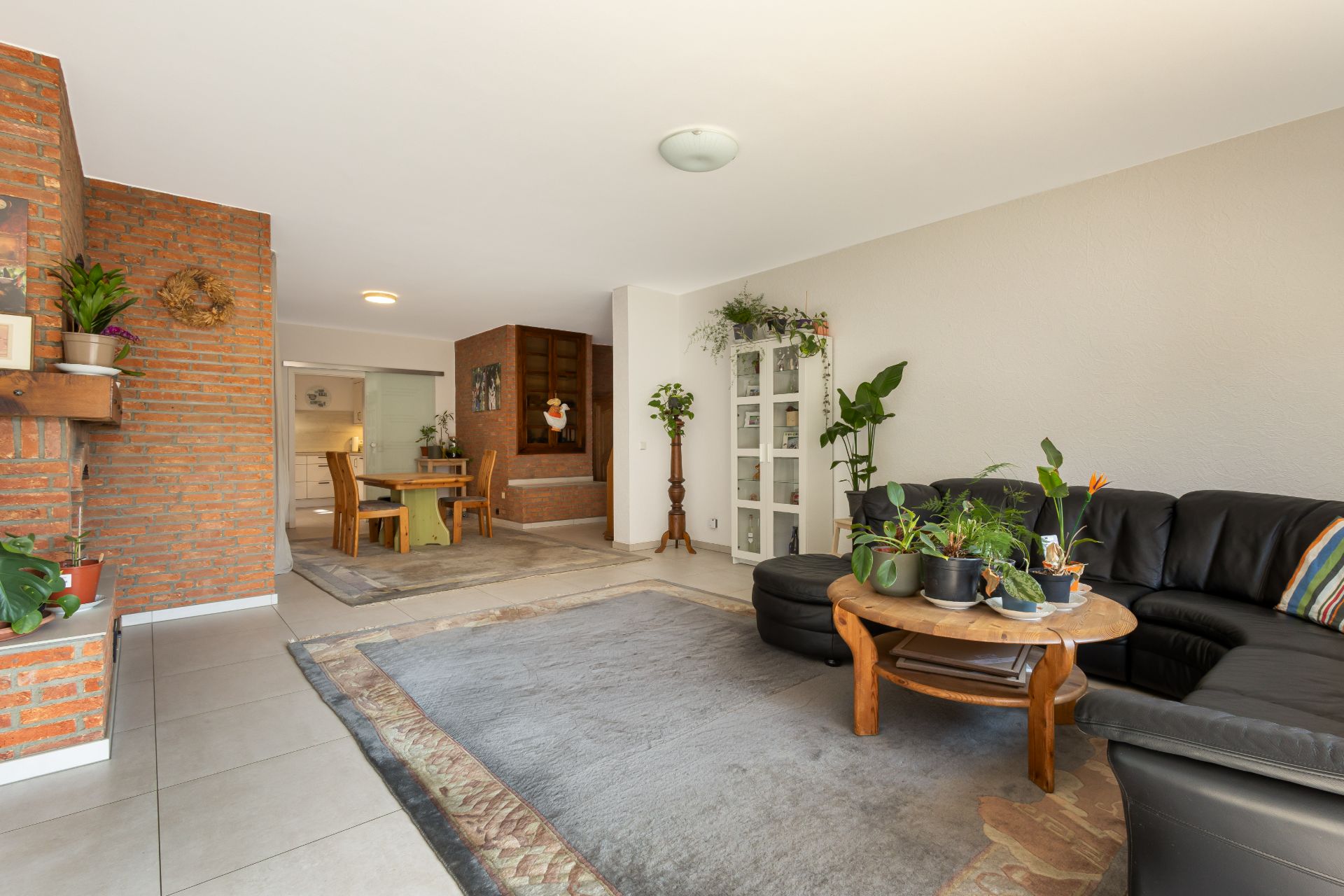 Helles Wohnzimmer mit schwarzem Sofa, Holztisch, Pflanzen und angrenzendem Essbereich.