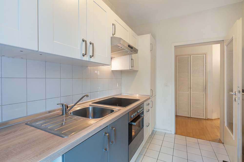 Moderne Küche mit Spüle, Herd, Backofen und weißen Schränken an den Wänden.