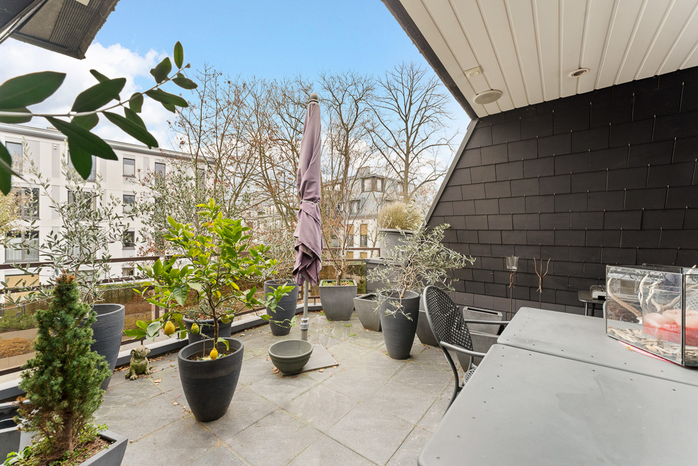 Überdachter Balkon mit vielen Pflanzen in Töpfen, Tisch, Stühlen und geschlossener Markise.